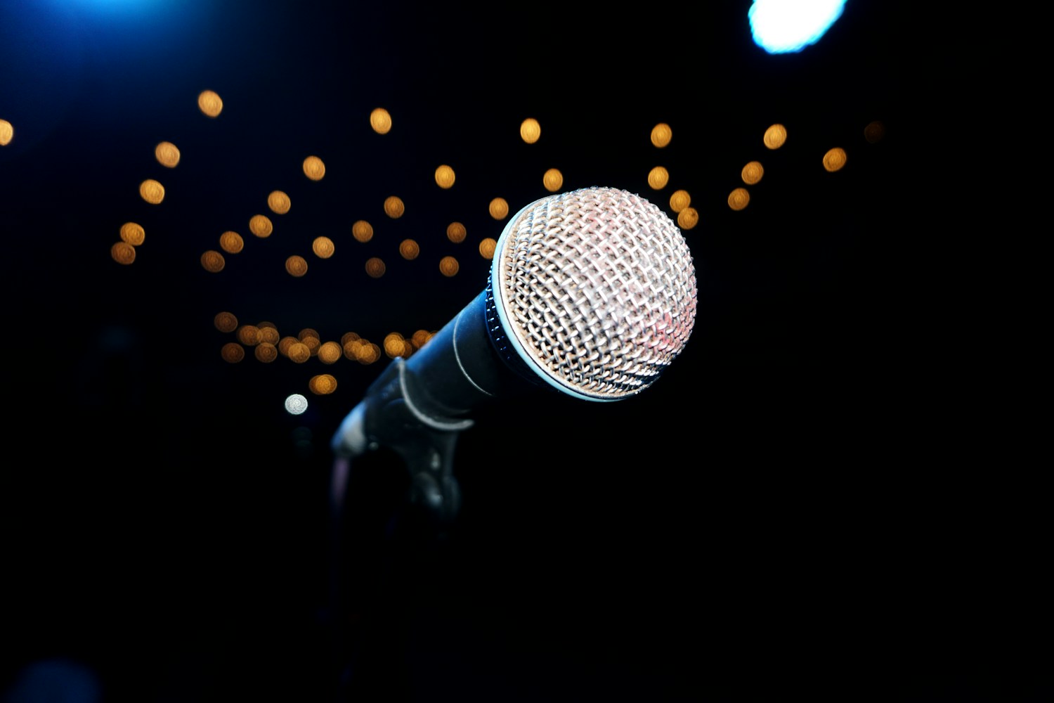Microfone em pedestal diante de um palco vazio com luzes desfocadas, imagem ilustrativa de comunicação e vendas